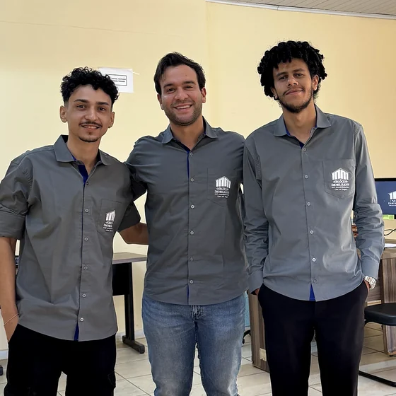 Os três diretores da 1001 lado a lado, da cintura para cima, com a camisa cinza da empresa, no escritório.